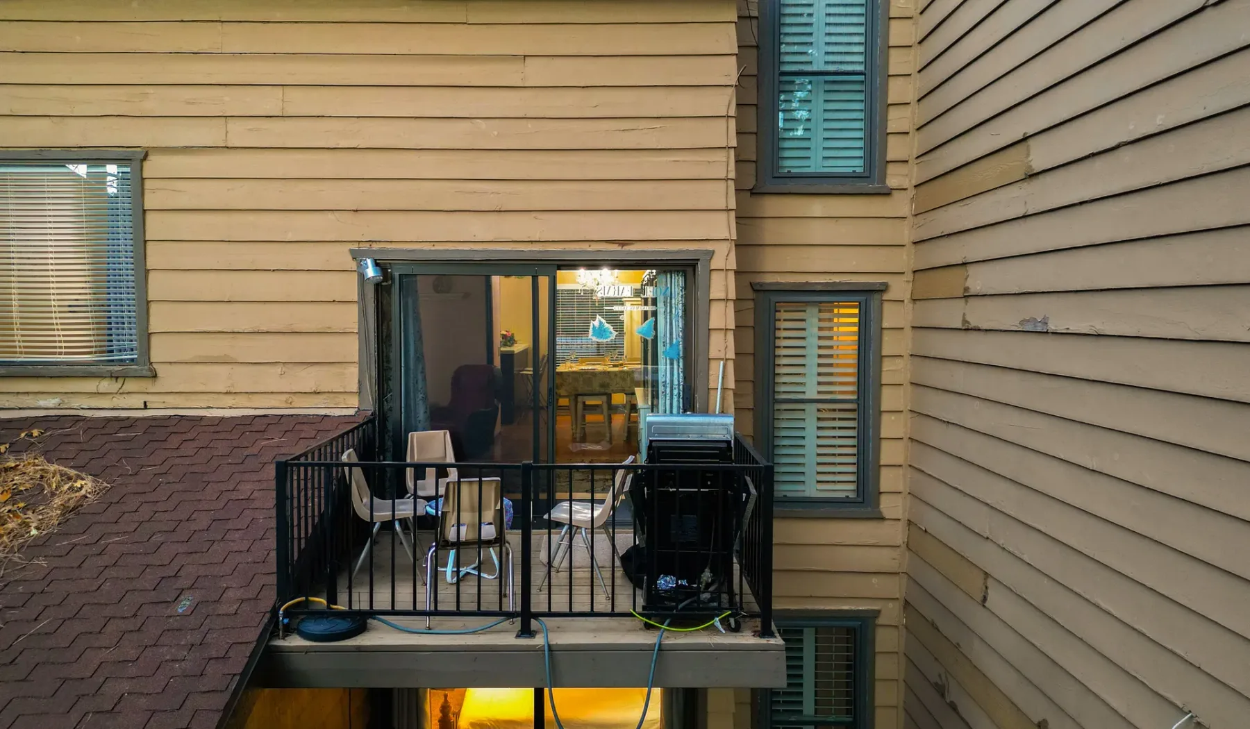 A small balcony with black railings is attached to a tan-sided building.