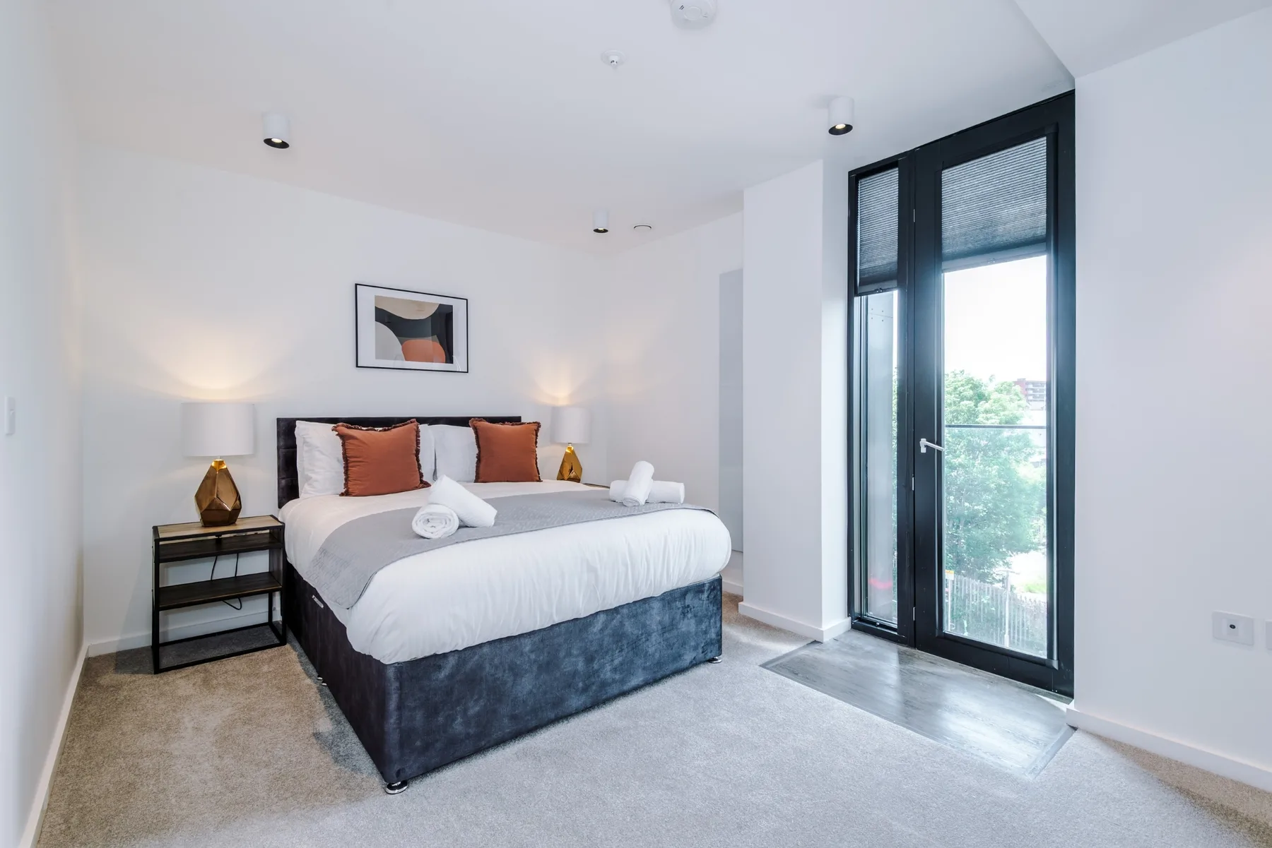 A bright bedroom with a neatly made bed beside tall glass doors.