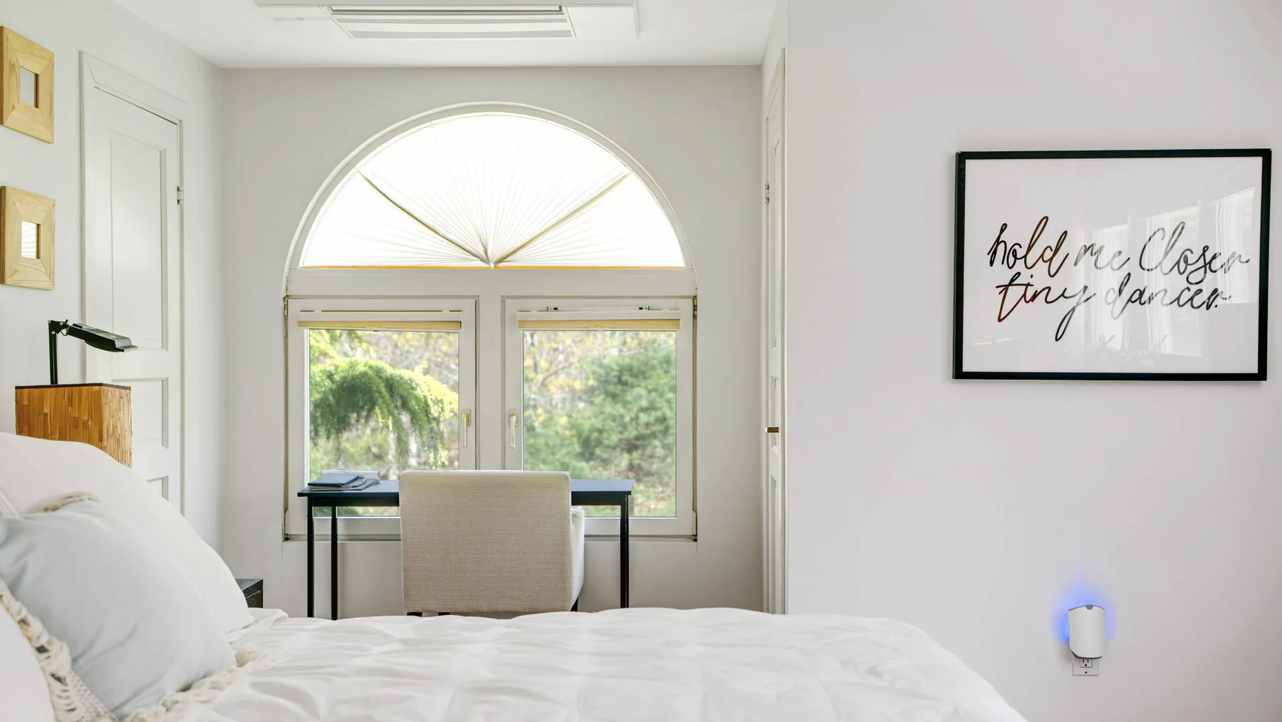 Un dormitorio luminoso con una cama frente a un escritorio bajo una ventana arqueada.