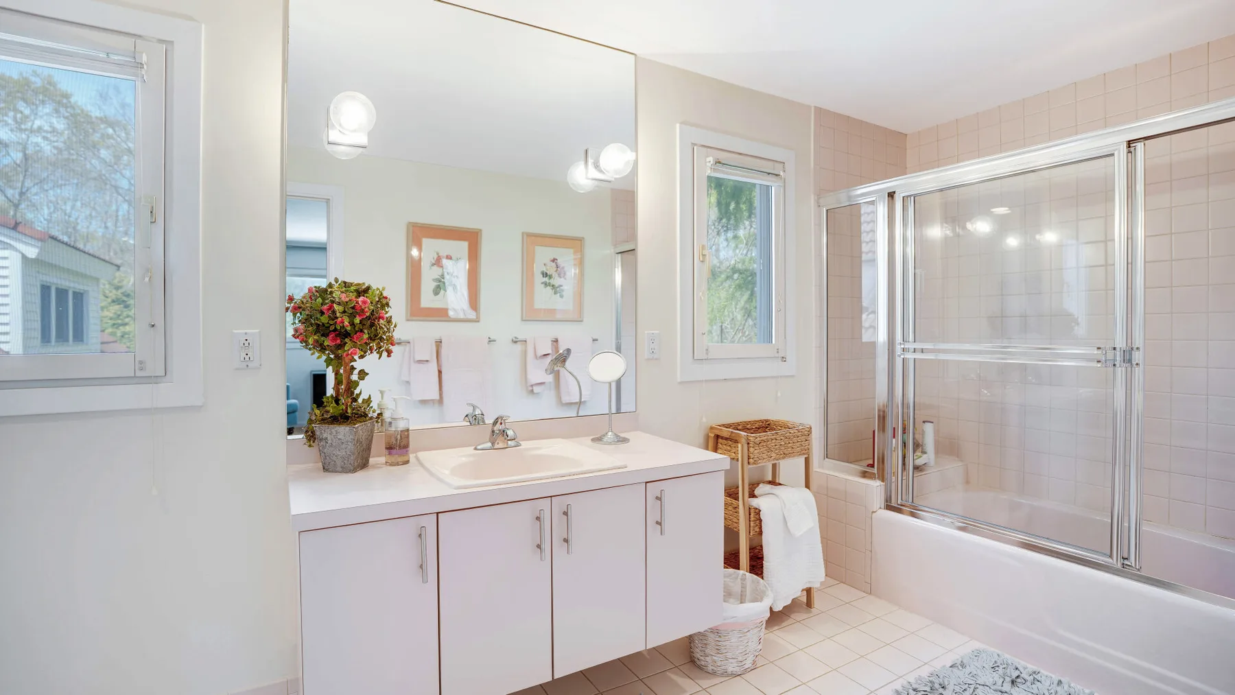 Un baño luminoso con lavabo, espejo y ducha con mampara de vidrio.