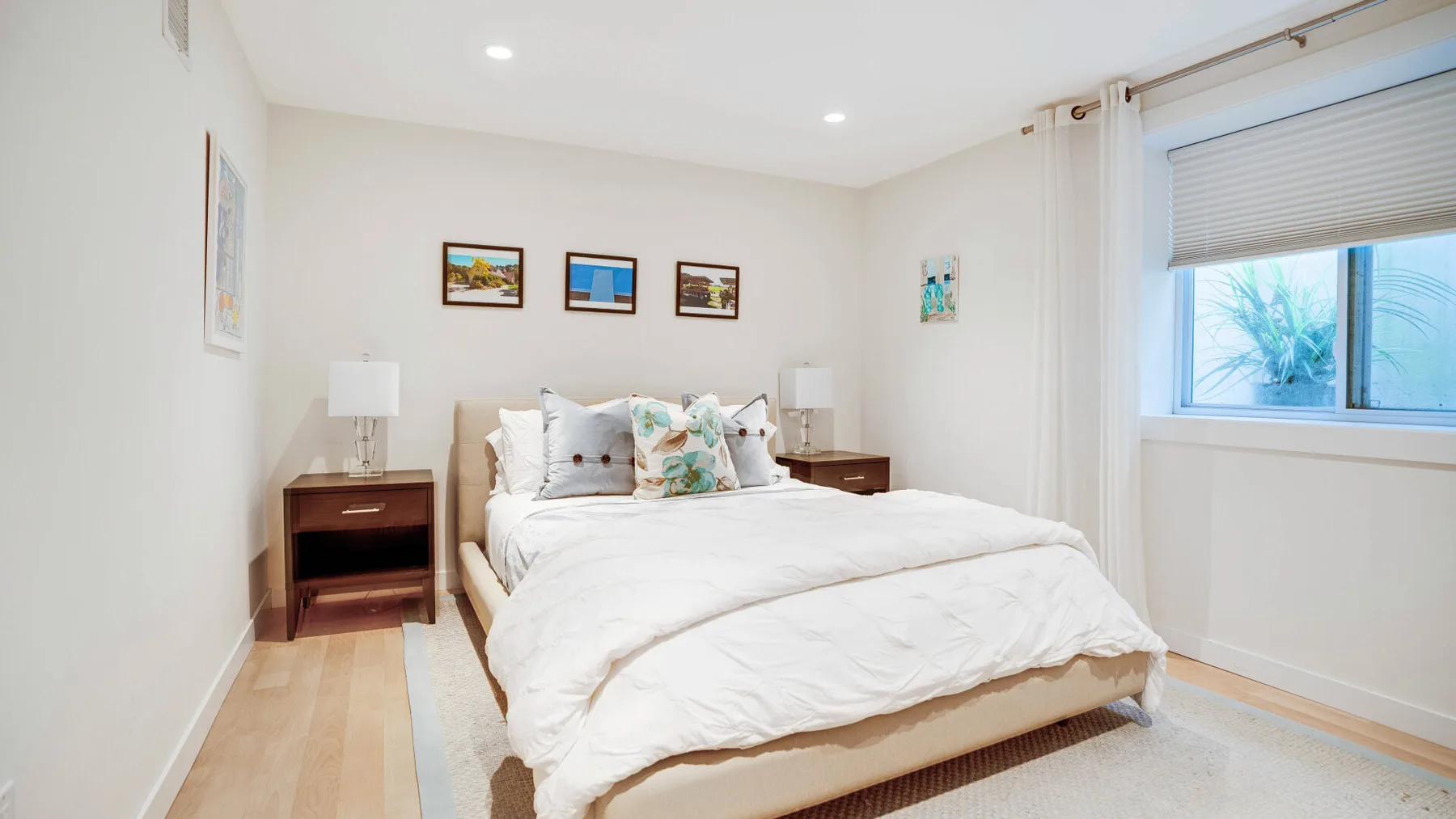 Un dormitorio luminoso con una cama tendida y cuadros en las paredes.