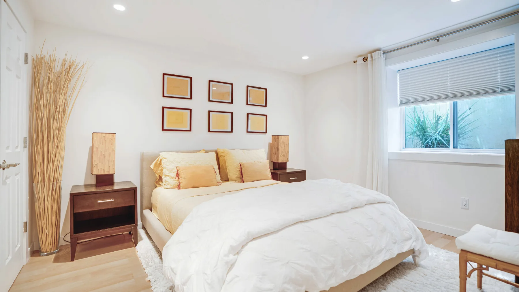 Un dormitorio luminoso con una cama y cuadros enmarcados sobre el cabecero.