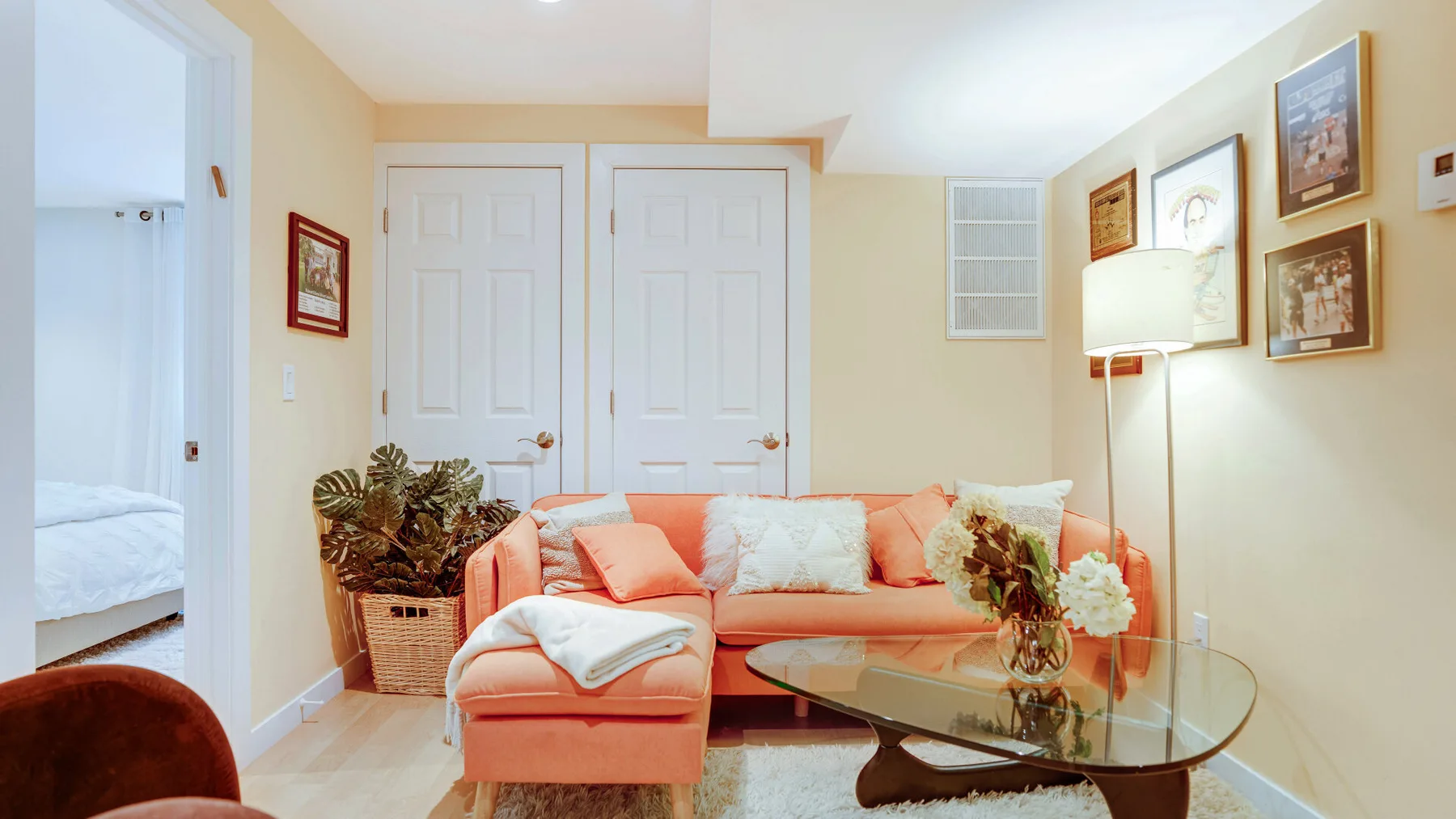 Una sala de estar con asientos color coral, una mesa de centro de vidrio y cuadros en la pared.