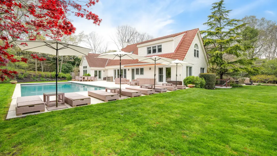 Una casa y un patio dan a una piscina y un amplio césped verde.