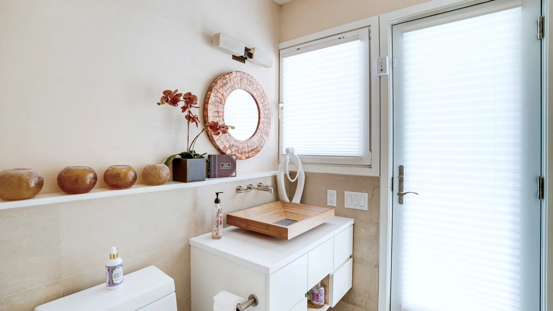 Un lavabo de baño luminoso está junto a una puerta y ventanas con persianas cerradas.