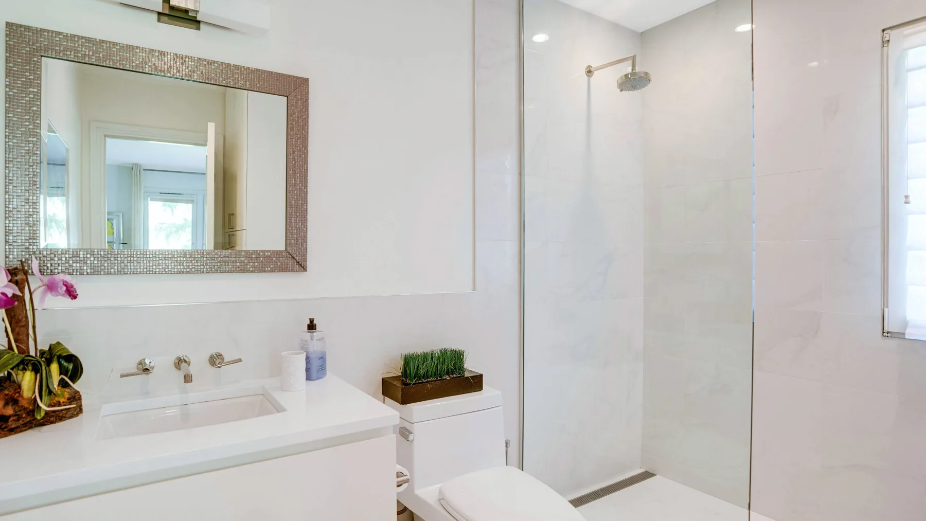Un baño luminoso con lavabo, espejo y ducha de vidrio.