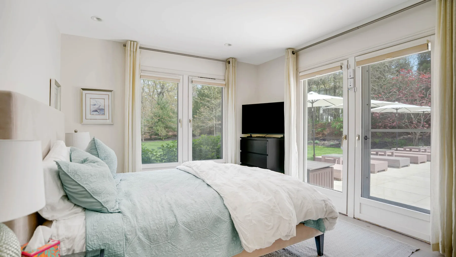 Un dormitorio luminoso con una cama junto a grandes ventanales con vistas a un jardín.