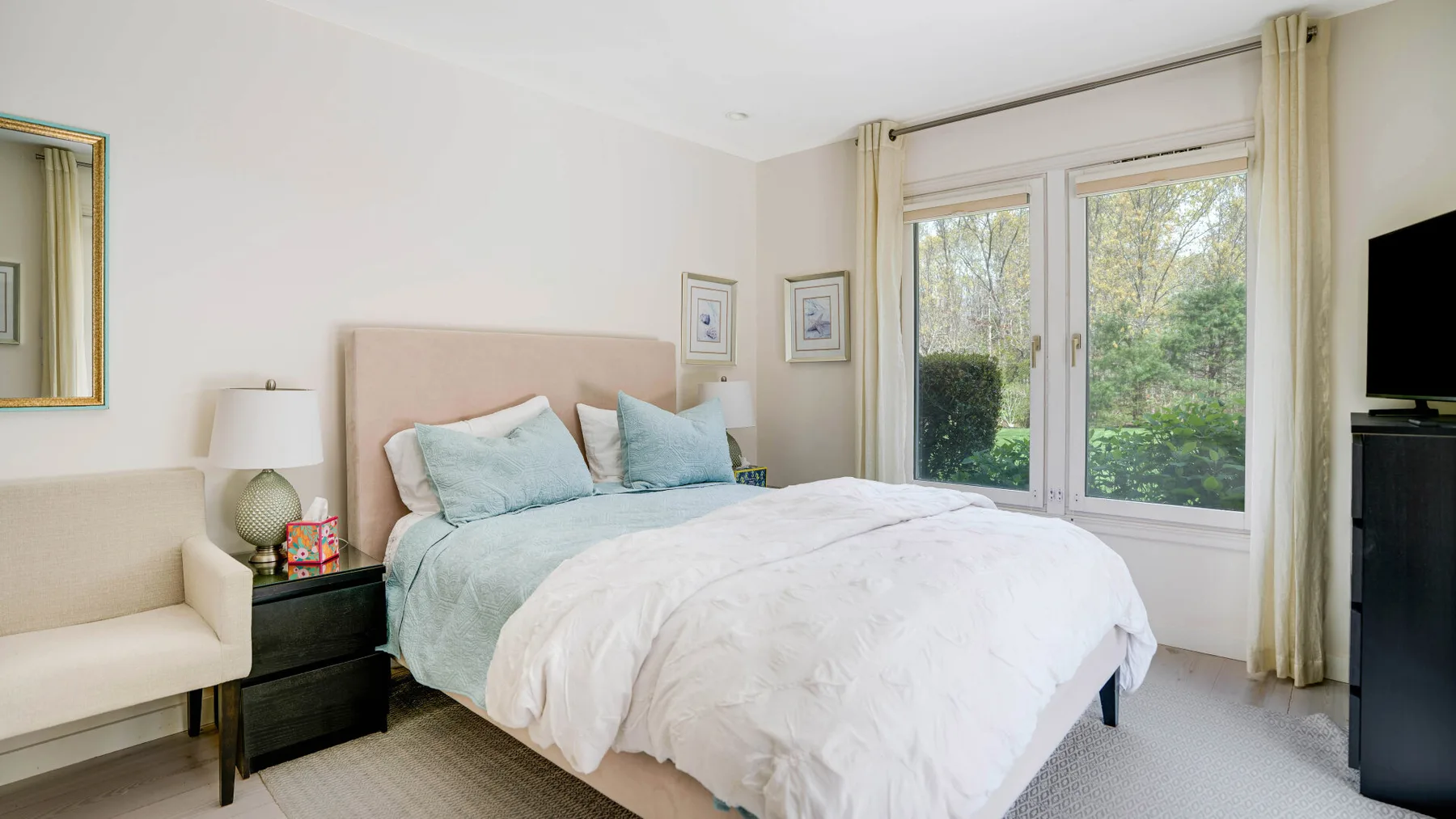 Un dormitorio luminoso con una cama junto a grandes ventanas con vistas a la vegetación.