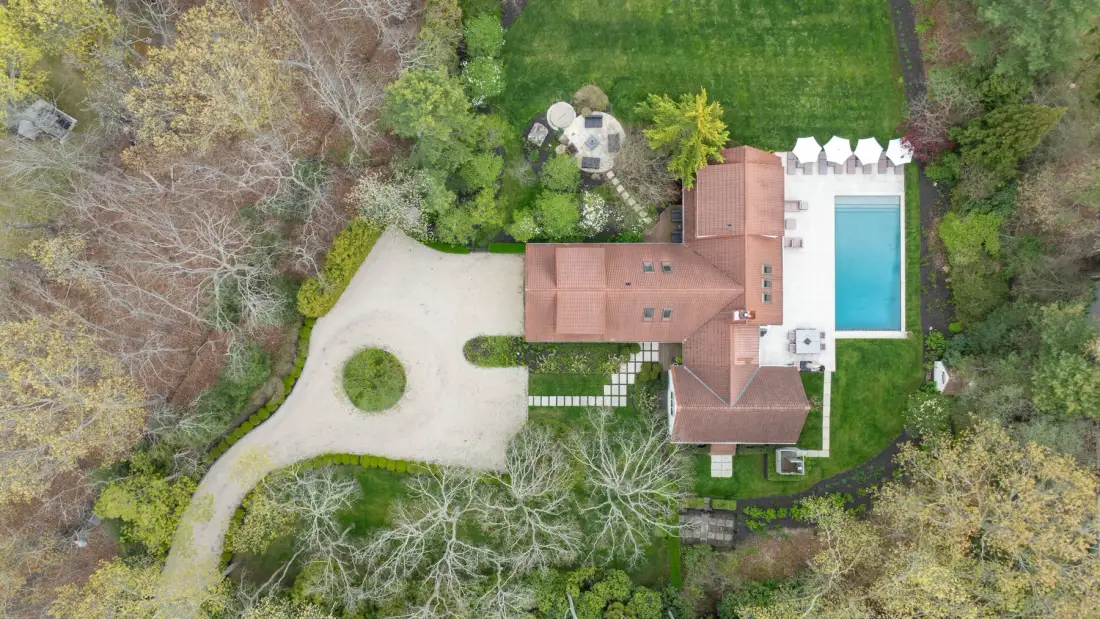 Una vista aérea muestra una casa, una piscina y jardines alrededor.