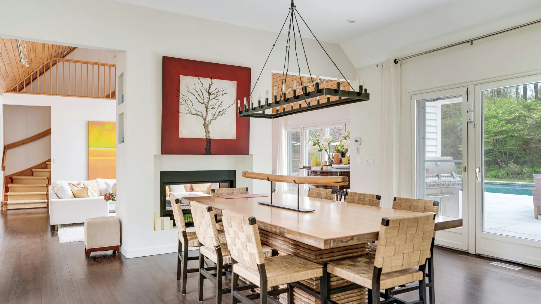 Un comedor luminoso con una mesa larga de madera junto a una chimenea y puertas de vidrio.
