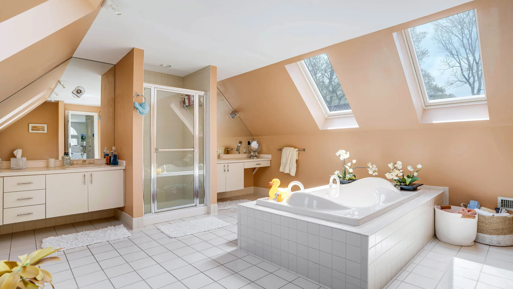 Un baño amplio tiene una bañera revestida de azulejos bajo ventanas inclinadas.