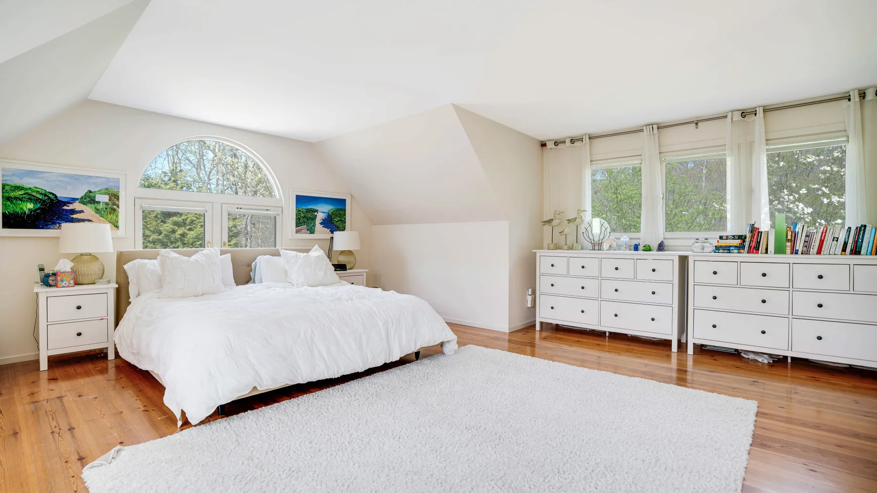Un dormitorio luminoso con una cama grande, una alfombra blanca y ventanas amplias.