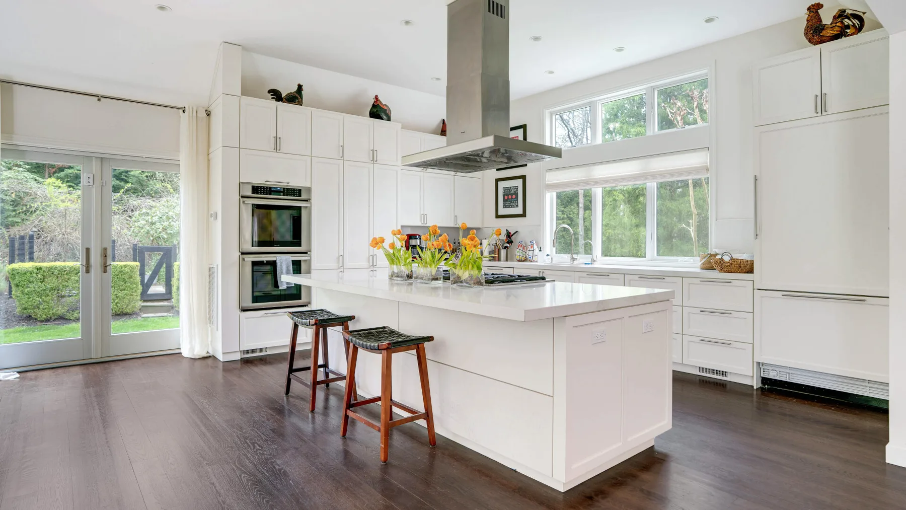 Una cocina blanca y luminosa con una isla central, ventanas y piso oscuro.
