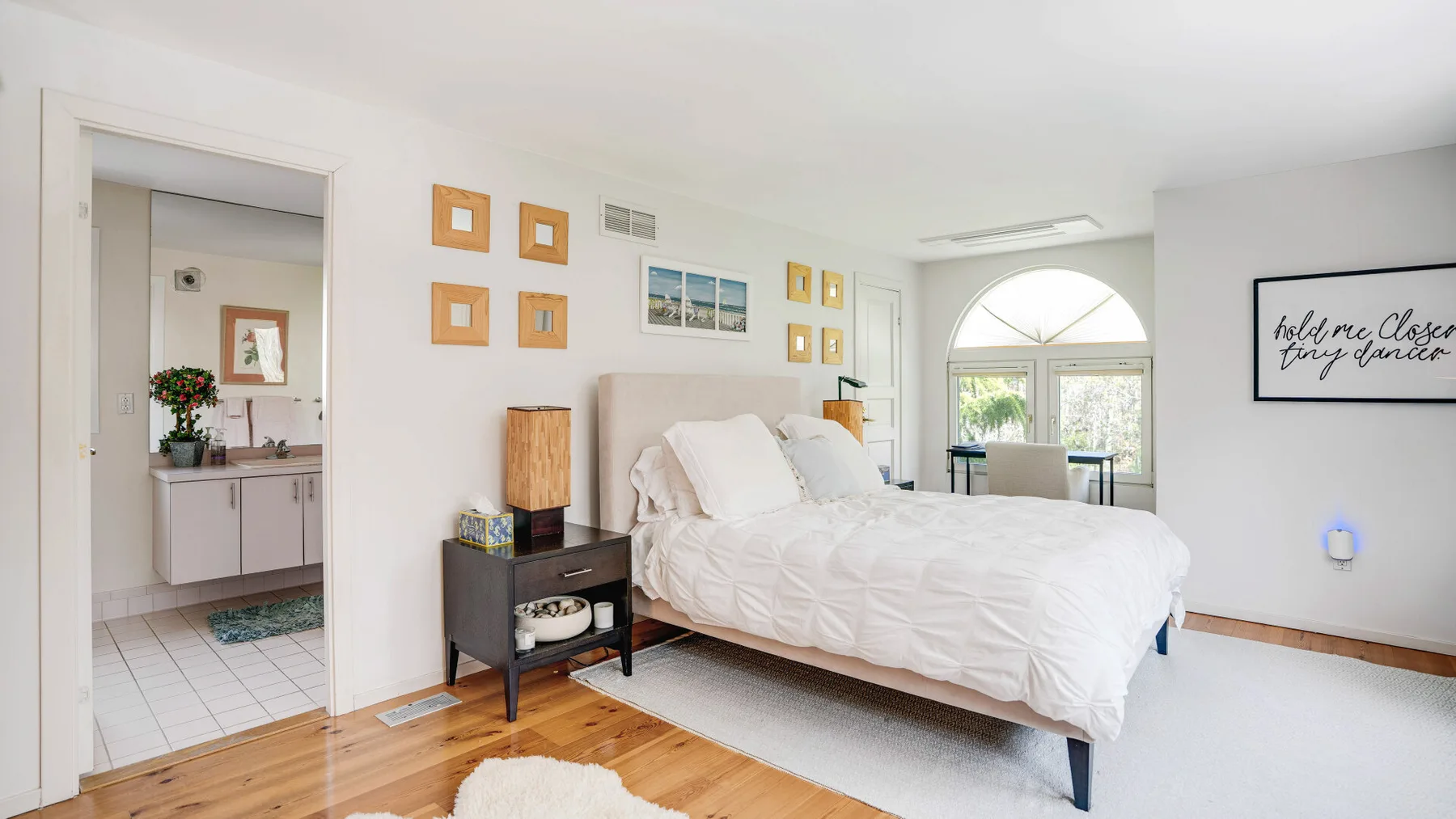 Un dormitorio luminoso con una cama blanca y una ventana arqueada.