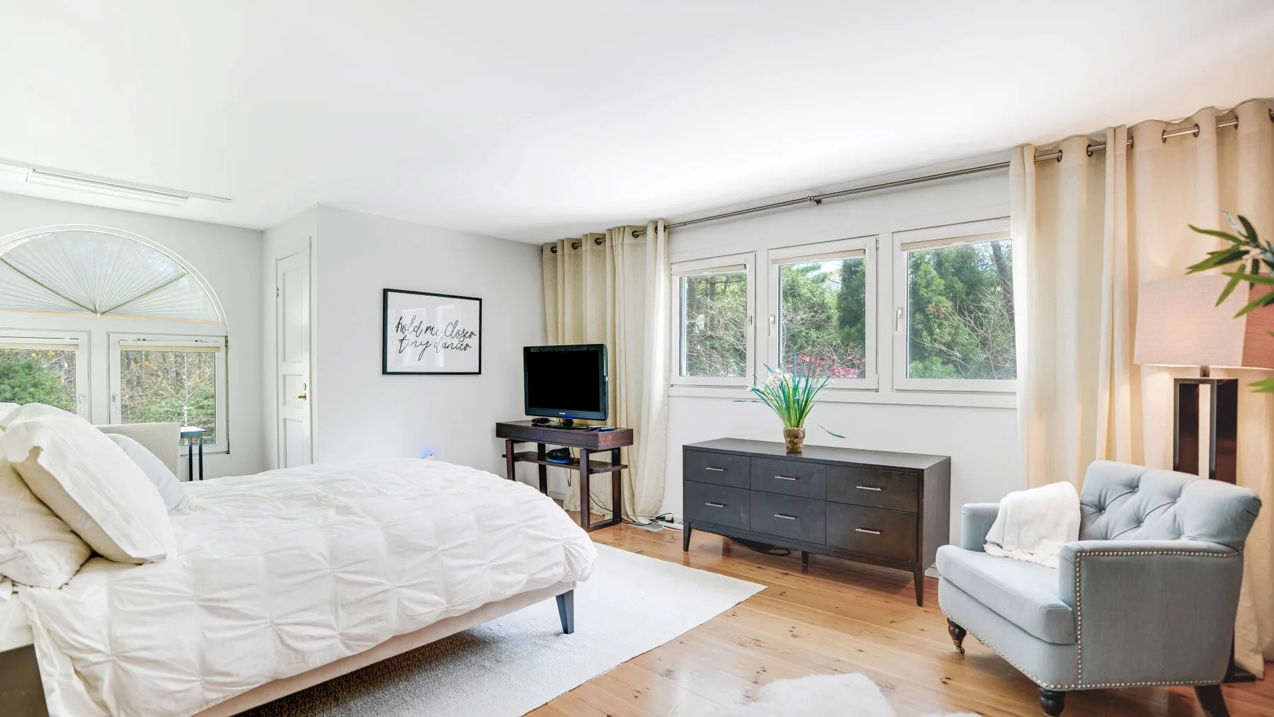 Un dormitorio luminoso con una cama grande, ventanas y una cómoda.