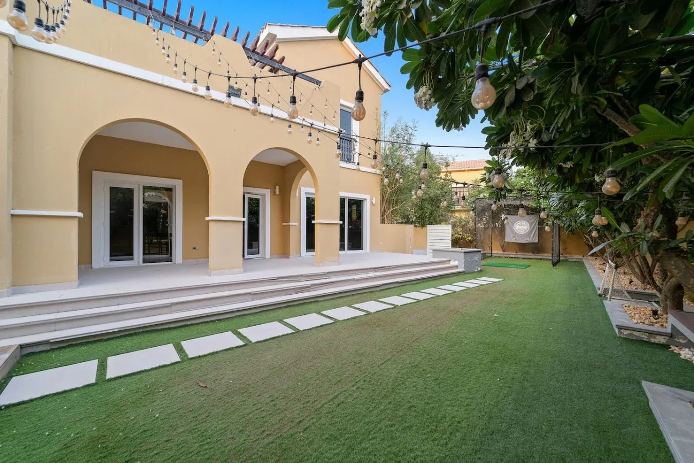 Un patio con césped verde, losas para caminar y un edificio con arcos.