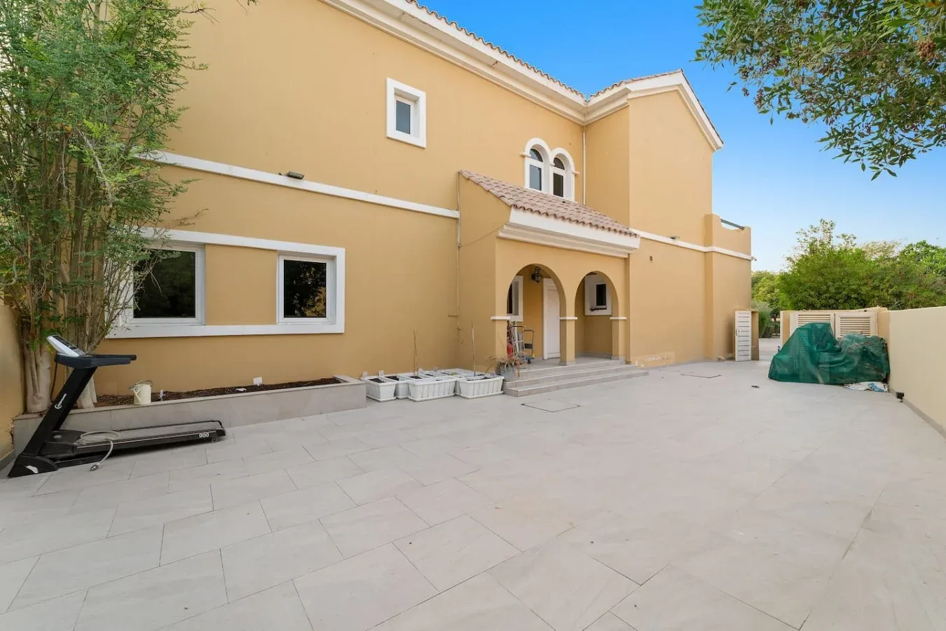 Un patio pavimentado se extiende frente a una casa amarilla con entradas arqueadas.