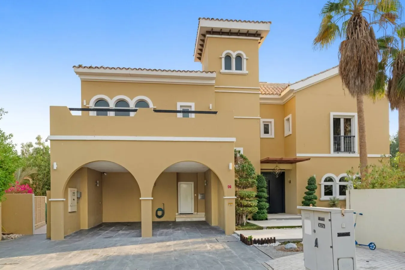 Una casa beige de estuco con entradas arqueadas, una torre y una palmera.
