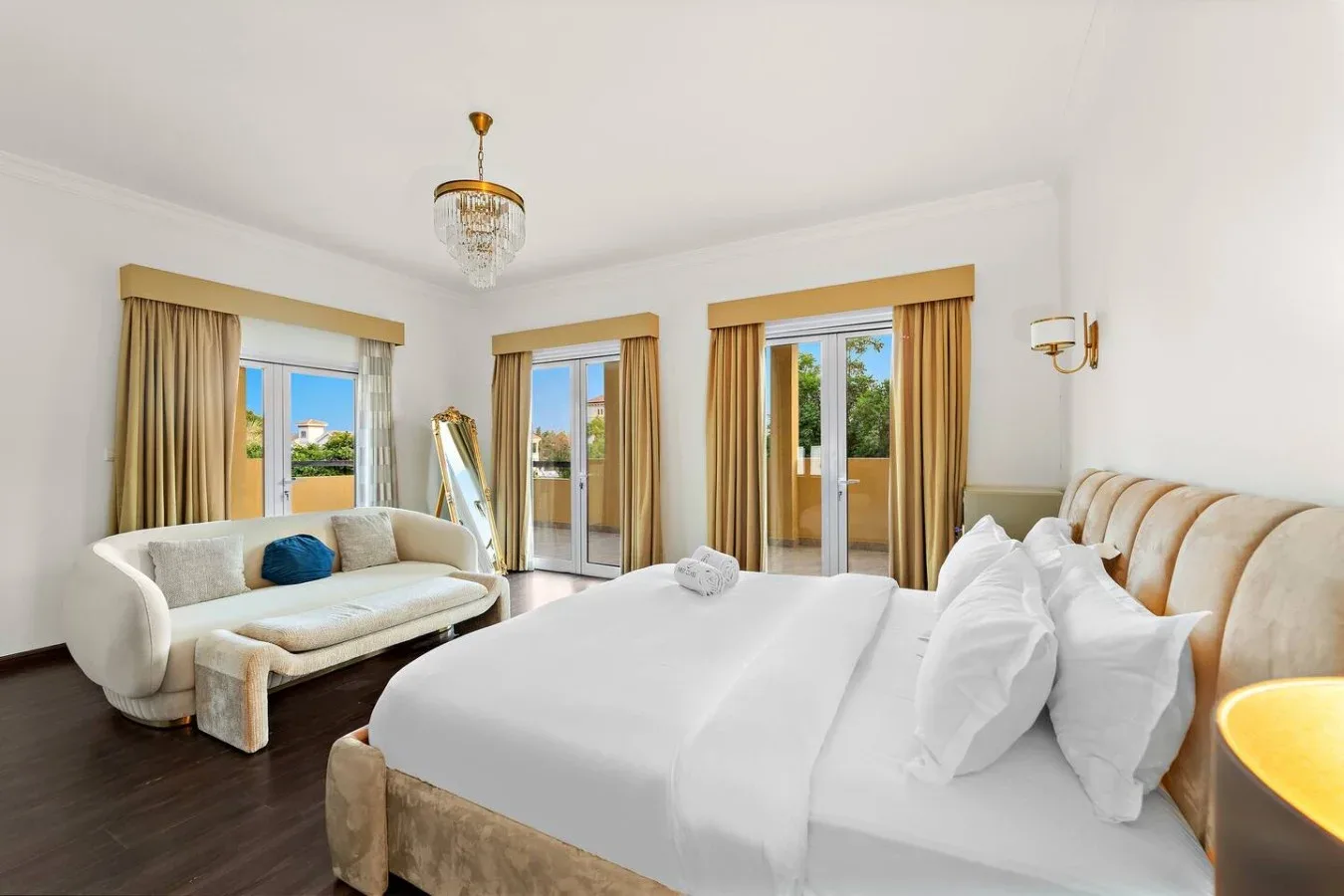 Un dormitorio luminoso con una cama grande y una pequeña zona de estar junto a las ventanas.