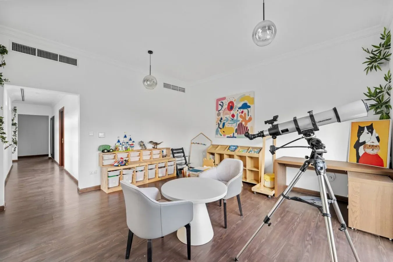 Una luminosa sala de juegos con mesas infantiles, estanterías y un telescopio.