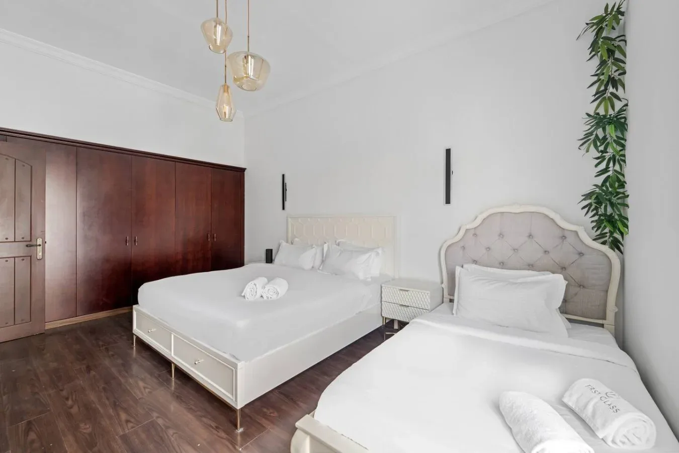 Un dormitorio luminoso con dos camas, suelo de madera oscura y un armario grande.