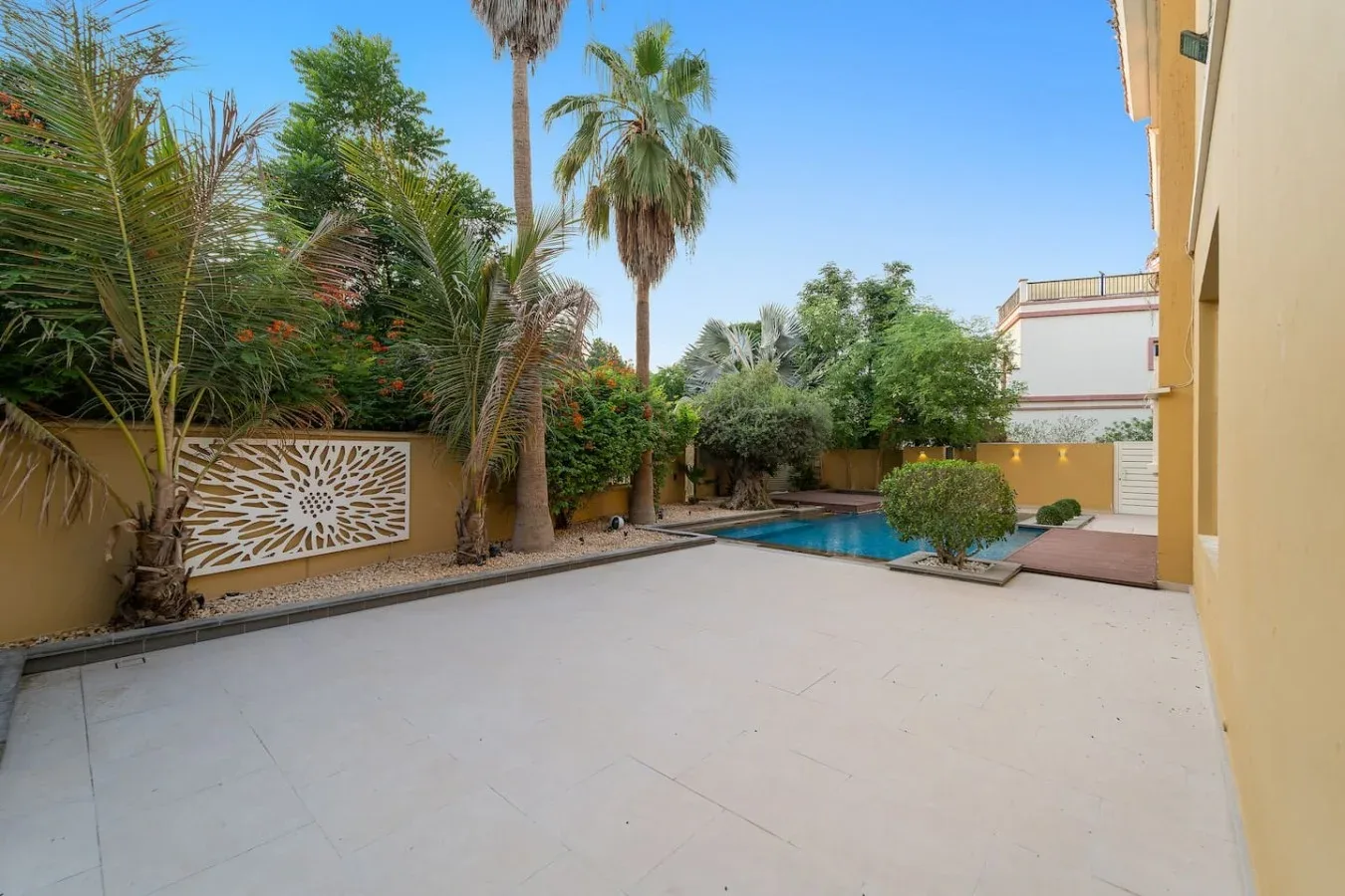 Un patio exterior pavimentado junto a una piscina y vegetación tropical.