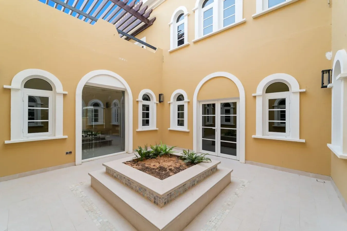 Un patio luminoso con ventanas arqueadas y un macetero central elevado.