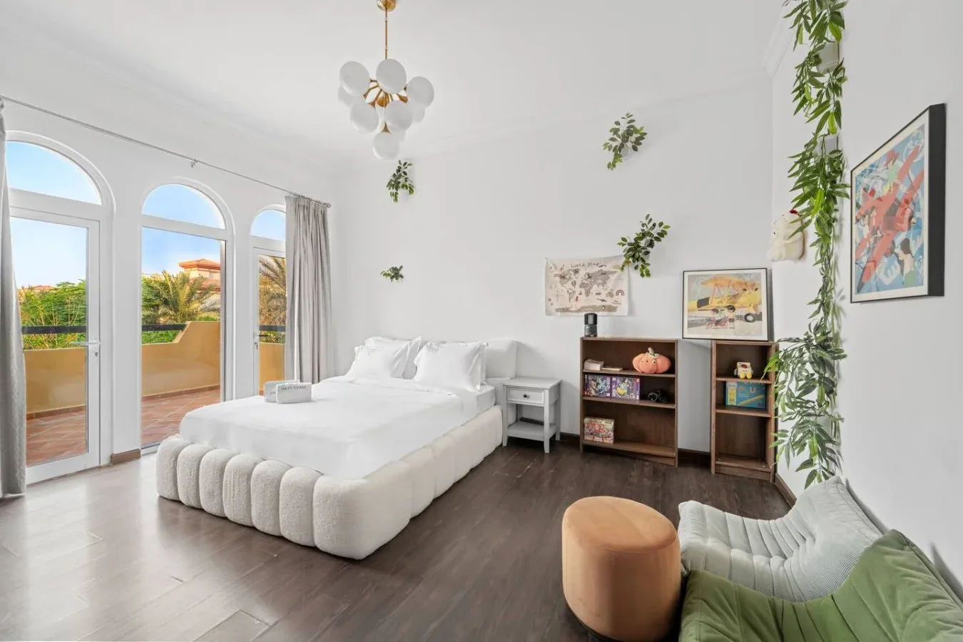 Un dormitorio luminoso con una cama blanca, ventanas altas y una pequeña zona de estar.