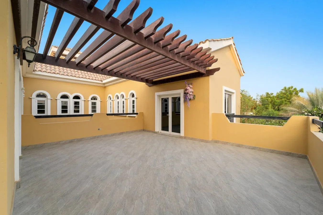 Una amplia terraza exterior con una pérgola de madera y ventanas arqueadas.