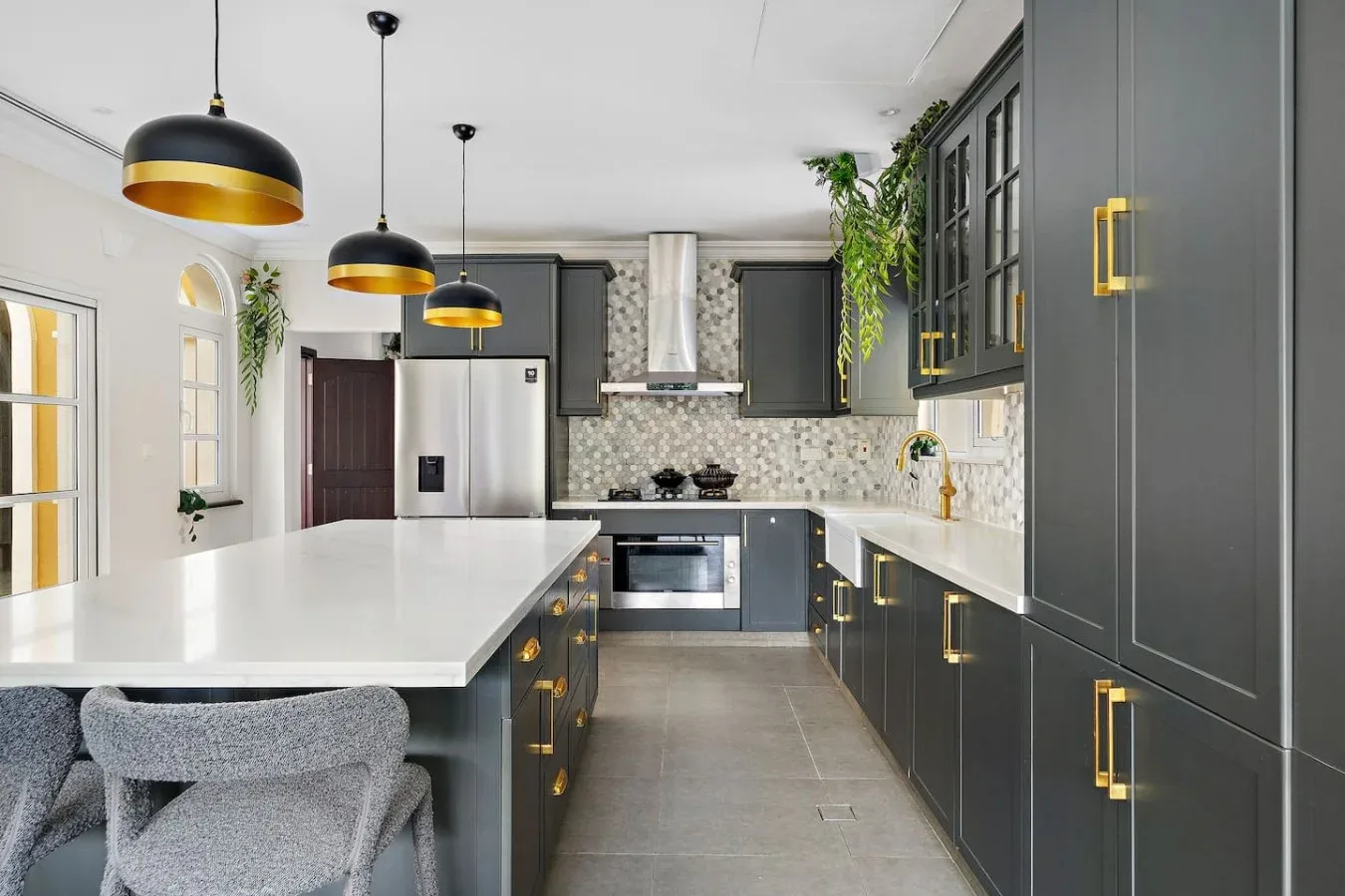 Una cocina moderna con gabinetes oscuros, encimeras blancas y lámparas colgantes.