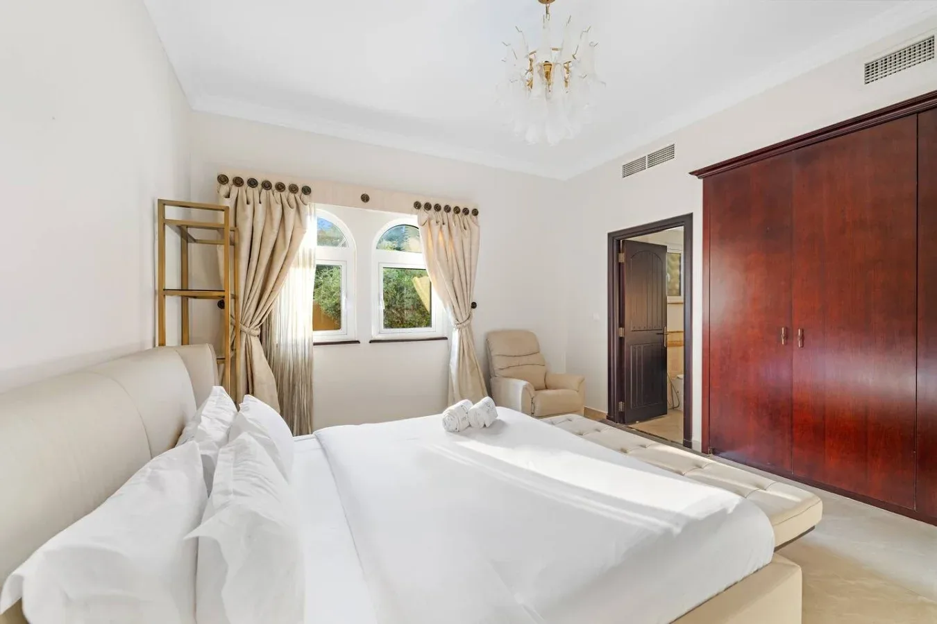 Un dormitorio luminoso con una cama grande, ventanas con cortinas y armarios de madera.