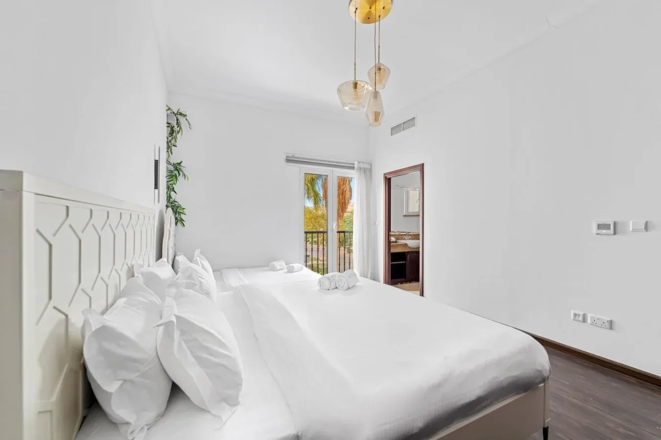 Un dormitorio luminoso con una cama bien tendida y ventanas altas.