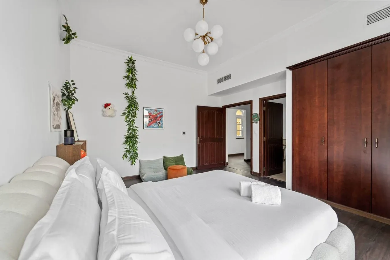 Un dormitorio luminoso con una cama blanca, un armario de madera oscura y una puerta abierta.