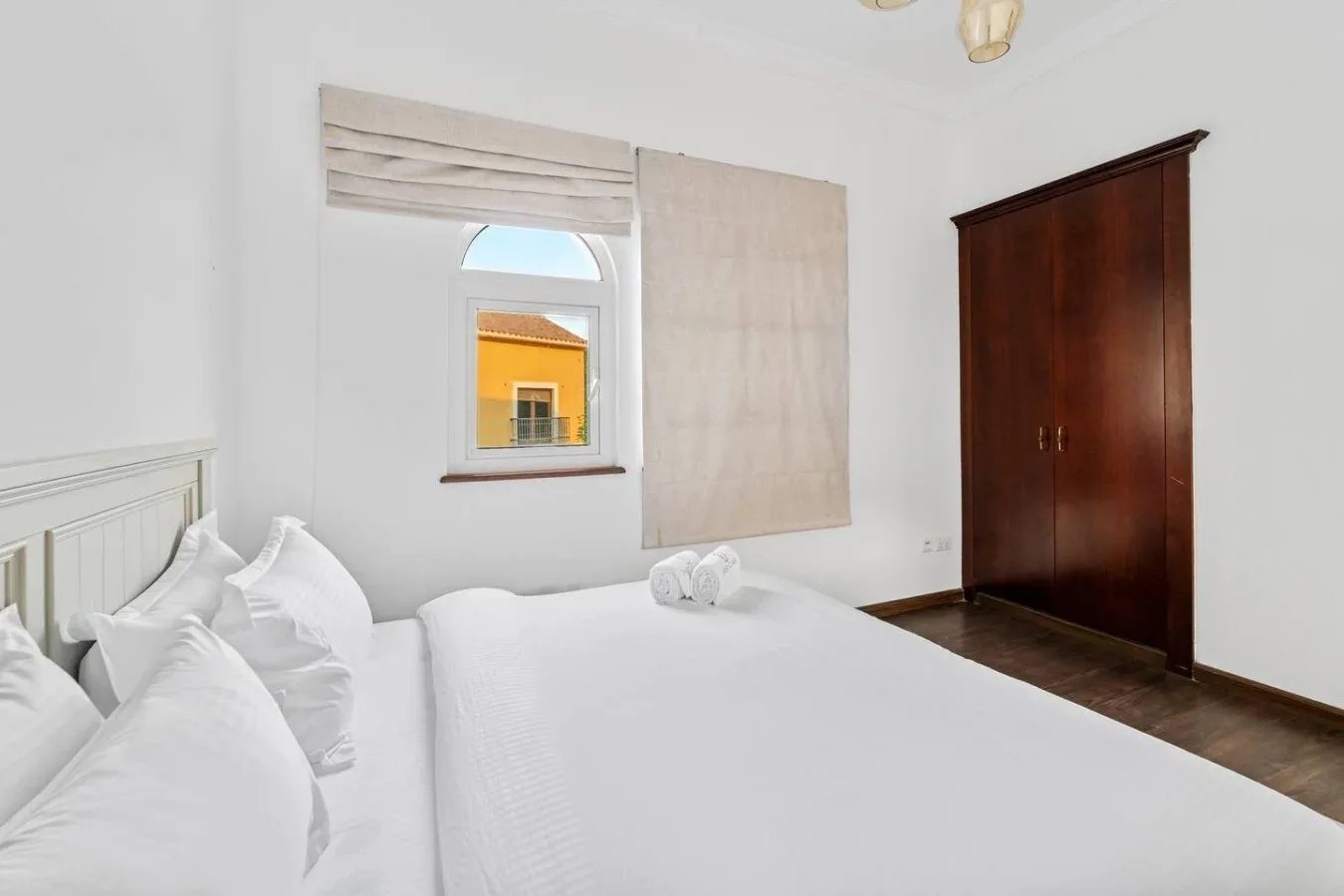 Un dormitorio luminoso con ropa de cama blanca, una ventana y un armario de madera oscura.