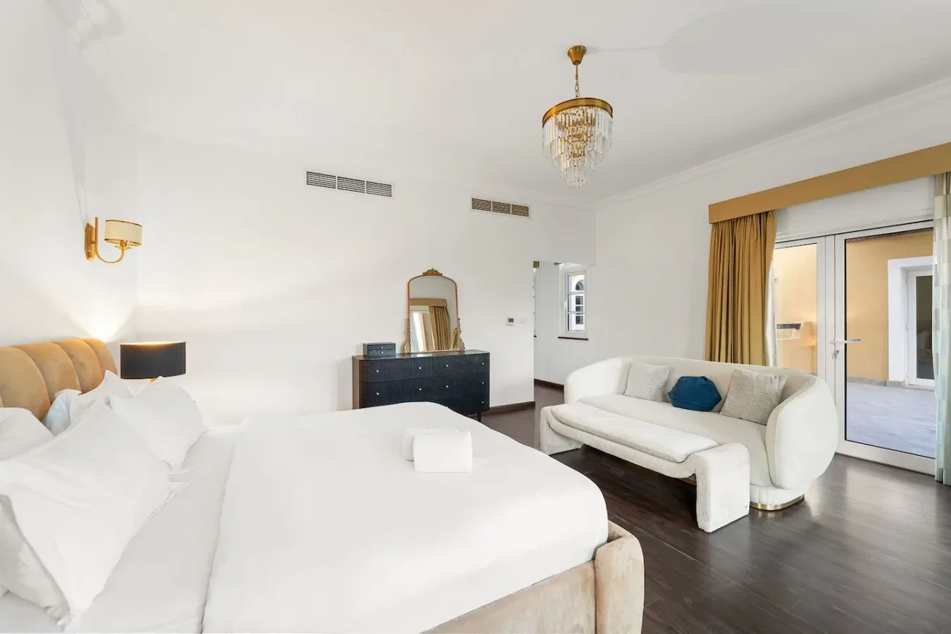 Un dormitorio luminoso con una cama grande y una zona de estar junto a puertas de vidrio.