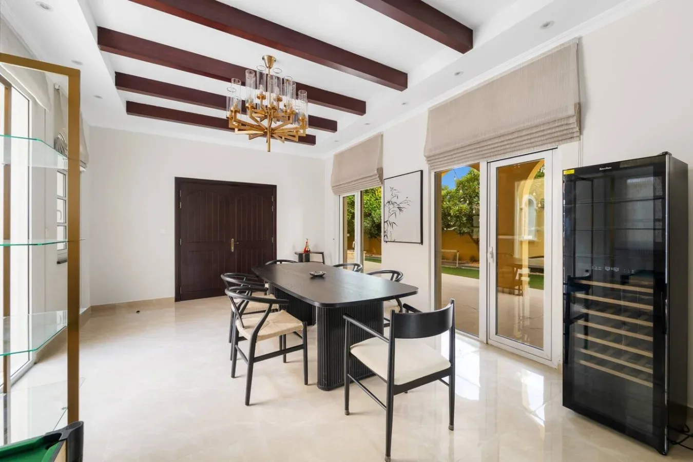 Un comedor luminoso con una mesa larga, vigas oscuras y puertas de vidrio.