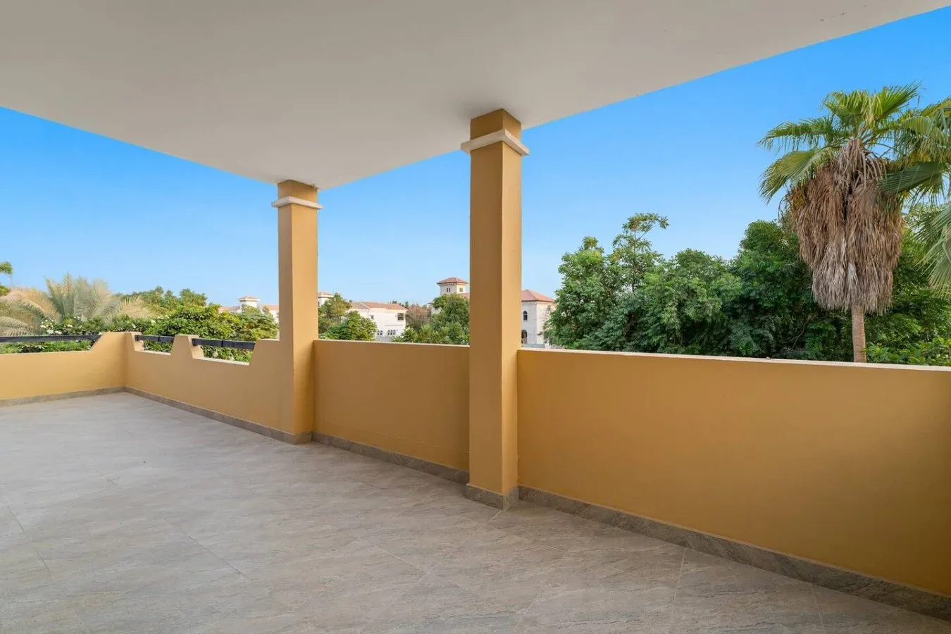 Una terraza cubierta con suelo de baldosas da a árboles y edificios cercanos.