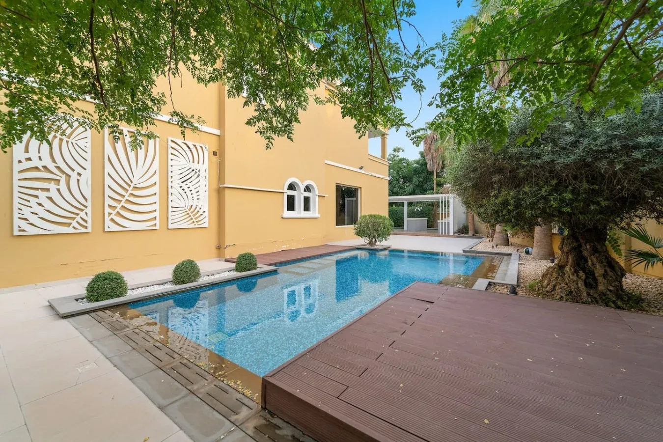 Una piscina al aire libre junto a un edificio amarillo, con árboles encima.