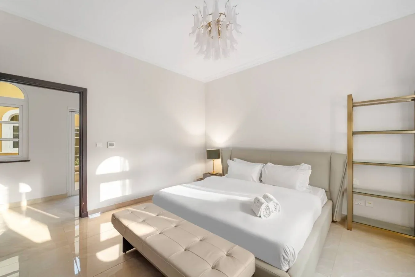 Un dormitorio luminoso con una cama blanca y un banco acolchado.