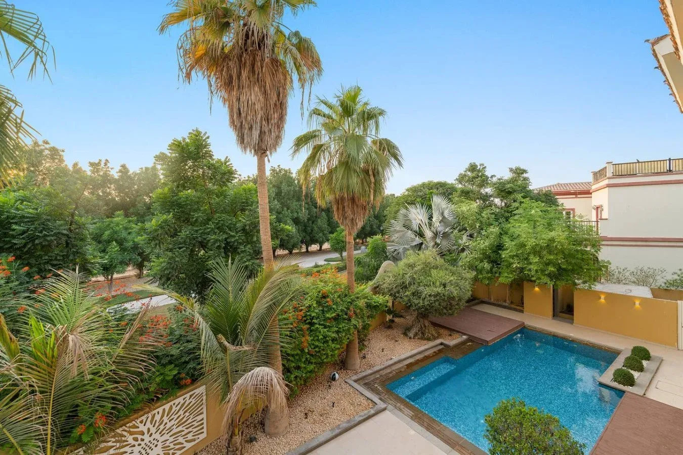 Una piscina está junto a un jardín con palmeras y arbustos.
