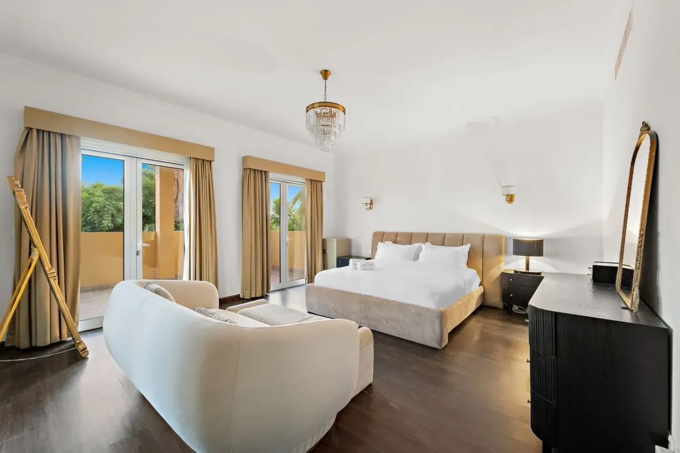 Un dormitorio luminoso con una cama grande, asientos y puertas de vidrio que dan a un balcón.