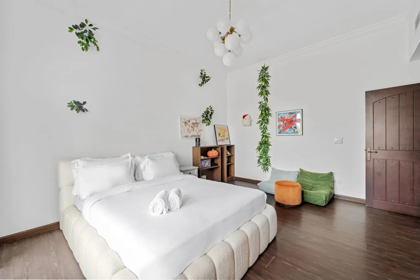 Un dormitorio luminoso con una cama blanca, asientos verdes y una puerta de madera.