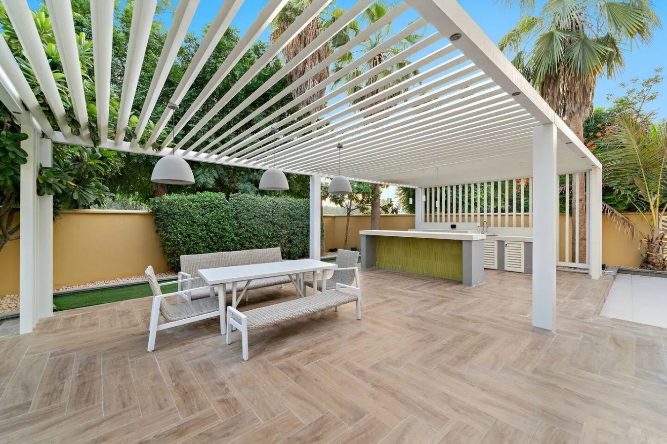 Un patio al aire libre con una pérgola blanca, asientos y una barra.