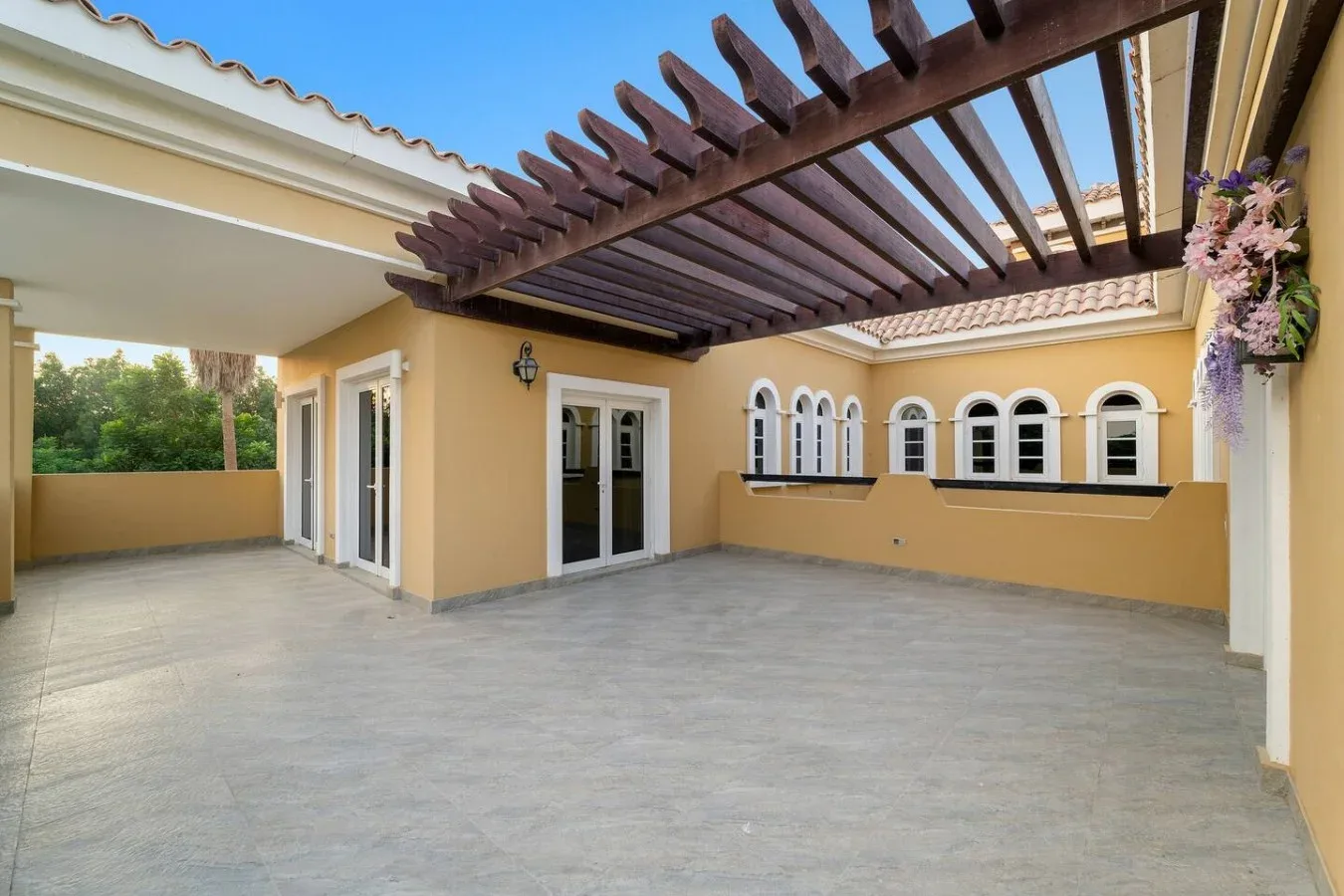 Una terraza exterior pavimentada con una pérgola de madera oscura junto al edificio.