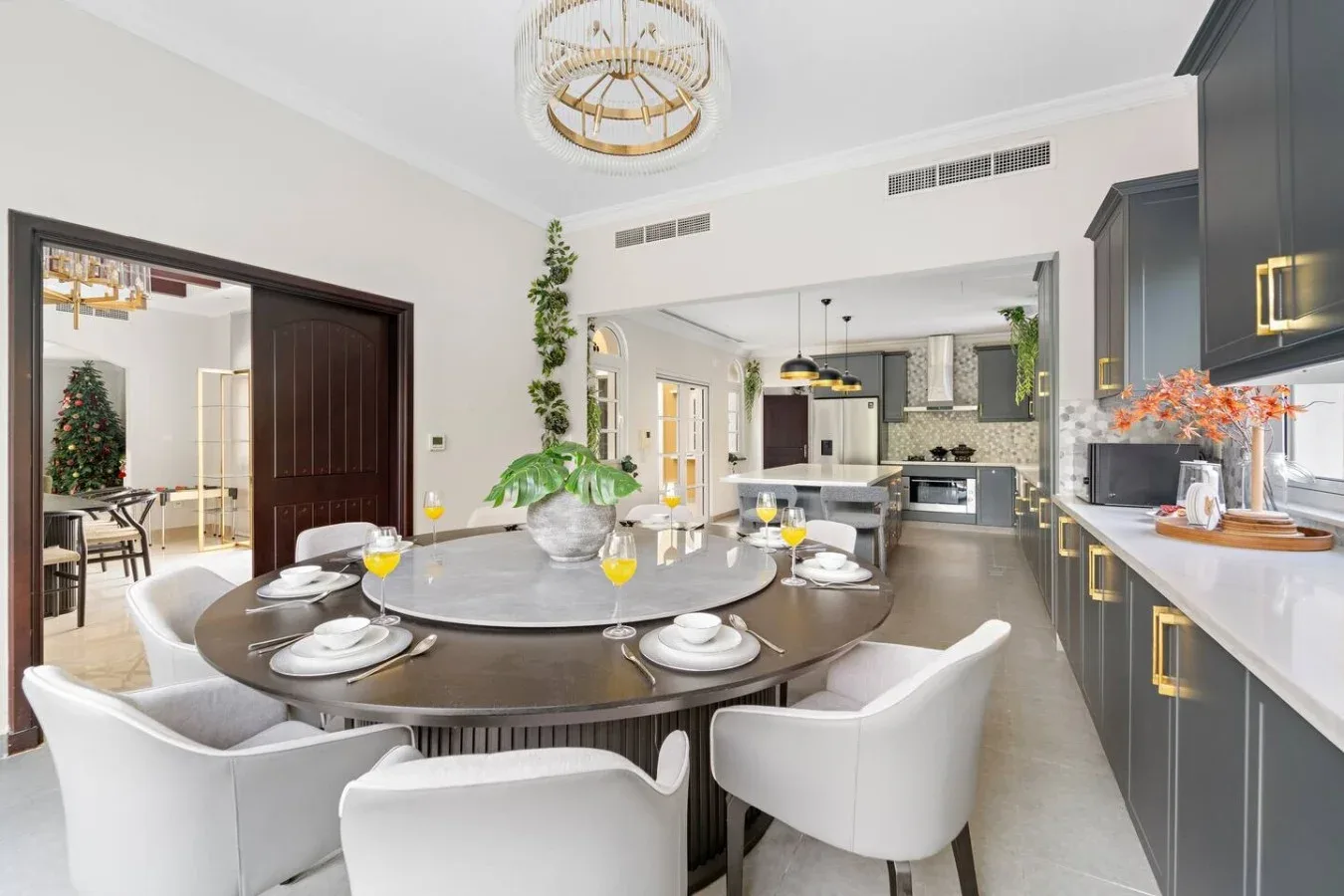 Un comedor con una mesa redonda y asientos blancos se abre a una cocina.