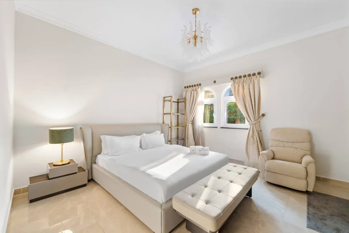 Un dormitorio luminoso con una cama bien hecha y un banco acolchado.