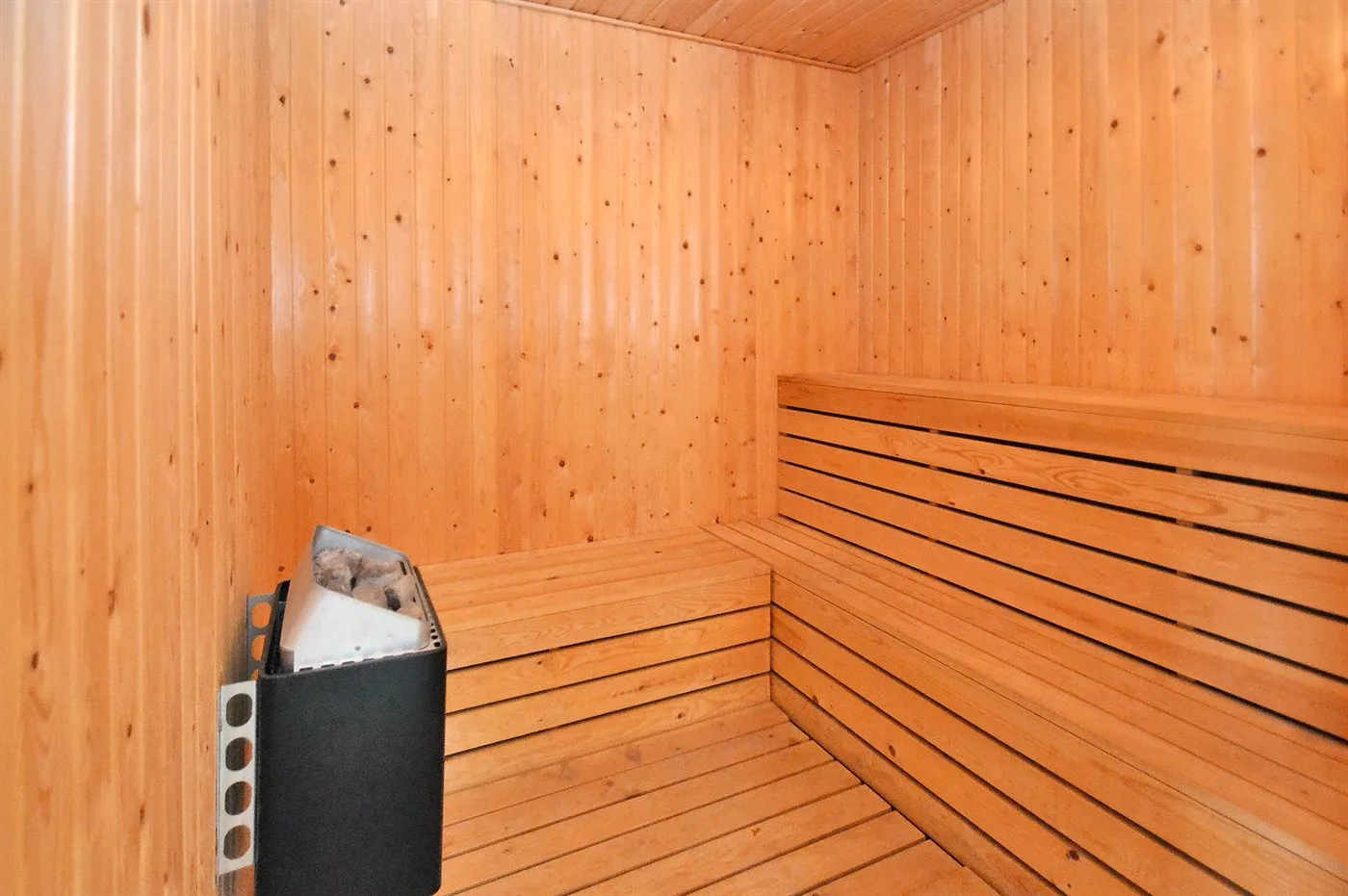 Una sauna revestida de madera con asientos escalonados y un calentador.