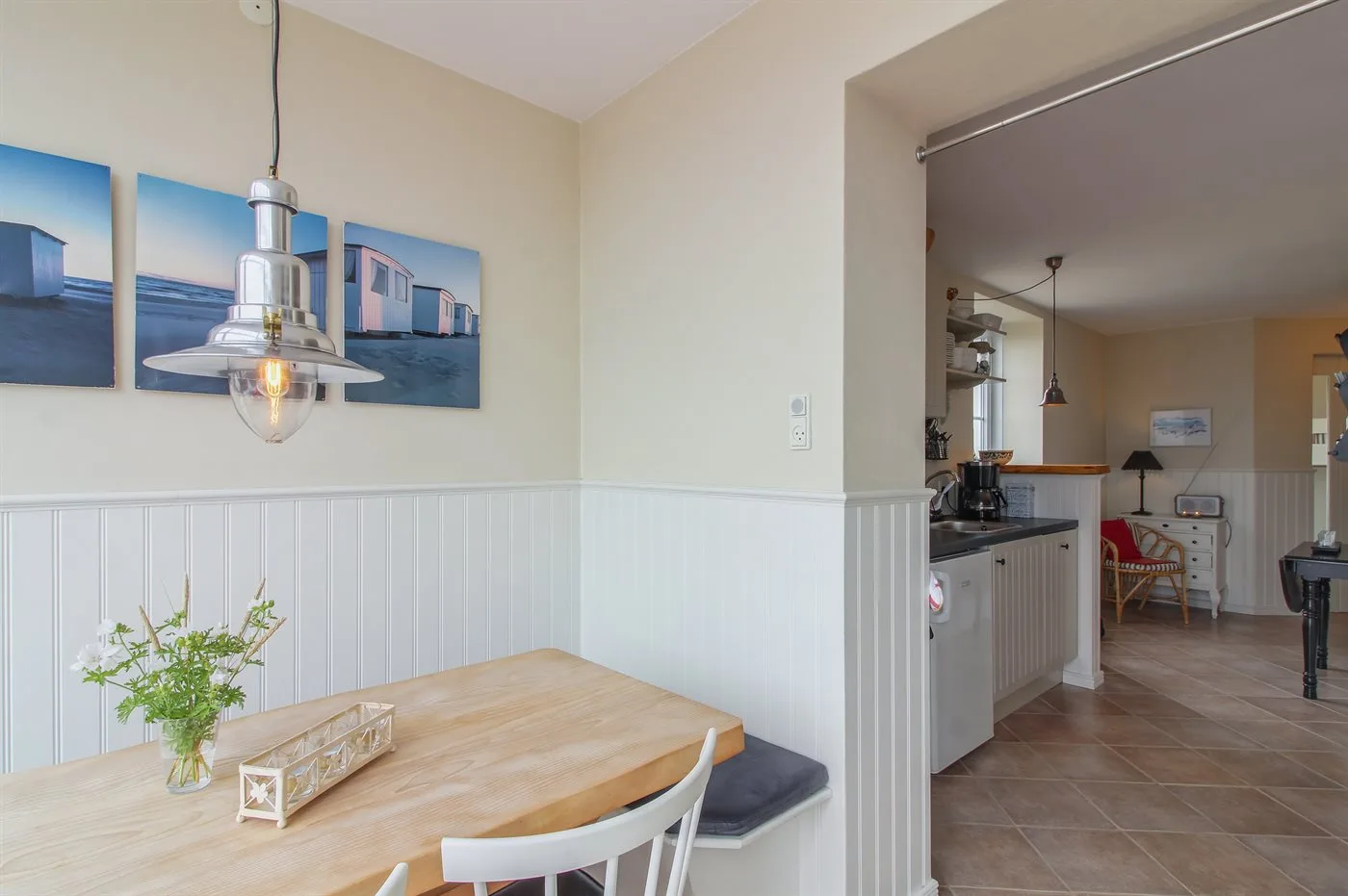 Un rincón de comedor con mesa de madera, cuadros y una cocina contigua.