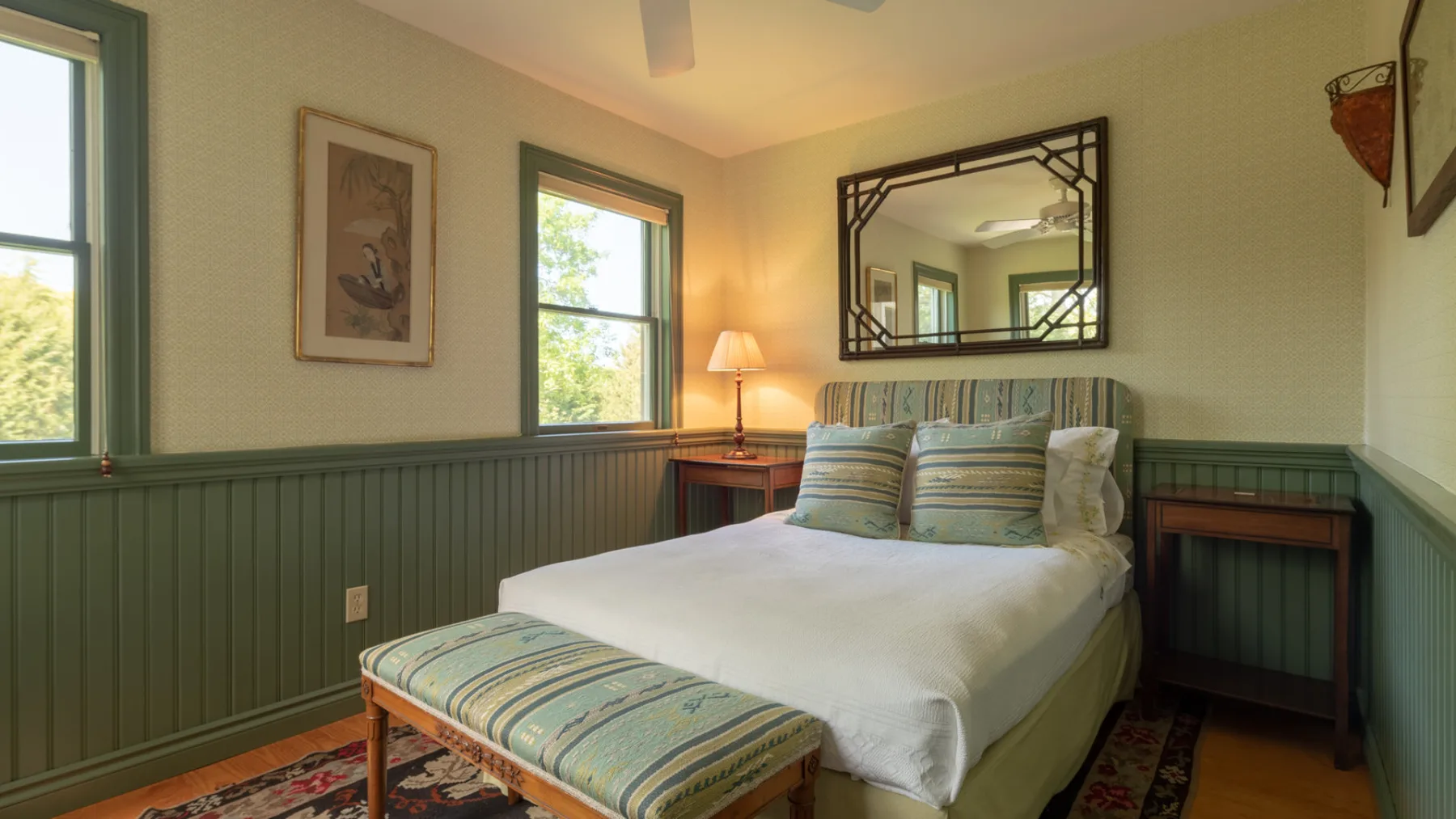 A bedroom with a neatly made bed and a striped bench at its foot.