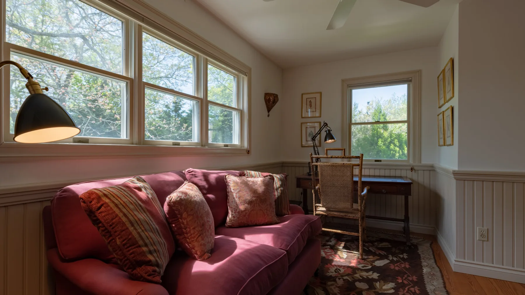 A sunlit sitting room with a burgundy sofa beside tall windows.